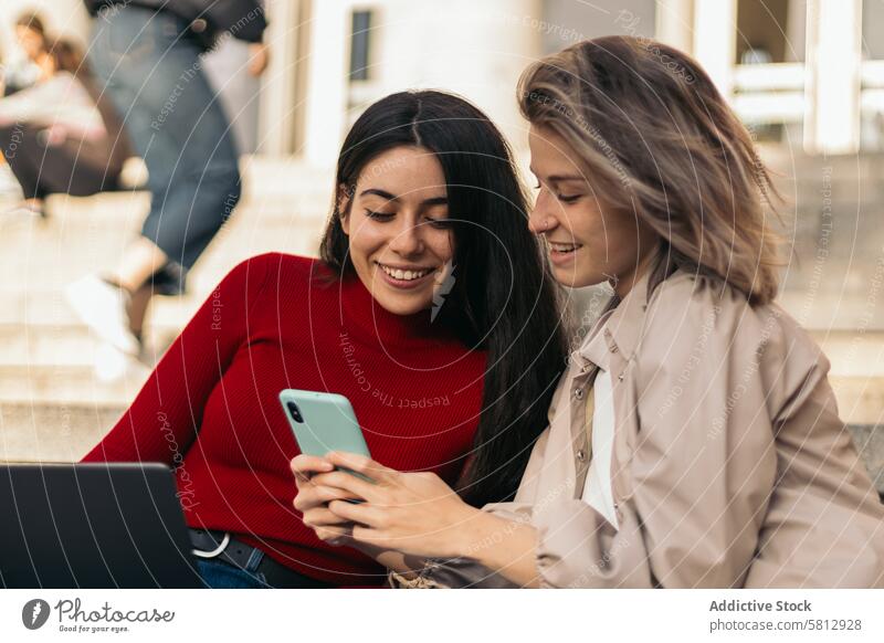 Zwei Studentinnen sitzen auf der Treppe des Colleges mit dem Laptop und dem Handy. Nahaufnahme jung Bildung Menschen Frau Computer zwei Mädchen Sitzen Mobile