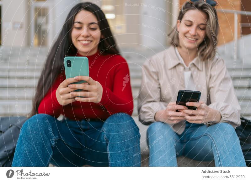 zwei Studentinnen sitzen auf der Treppe und beobachten das Handy jung Freunde Telefon Mobile Mädchen Frau Internet Schüler Menschen Paar Smartphone Glück