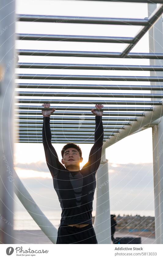 Ethnischer Sportler beim Training auf dem Affenbarren Affenstangen Übung Athlet Aktivität Fitness Sonnenuntergang Bestimmen Sie Turner jung Mann asiatisch