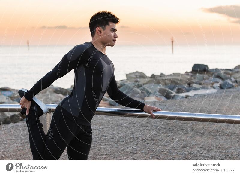 Ethnischer Sportler bei Dehnungsübungen am Meeresufer Mann Training Fitness Übung sportlich Aufwärmen Sonnenuntergang MEER asiatisch ethnisch männlich Bein