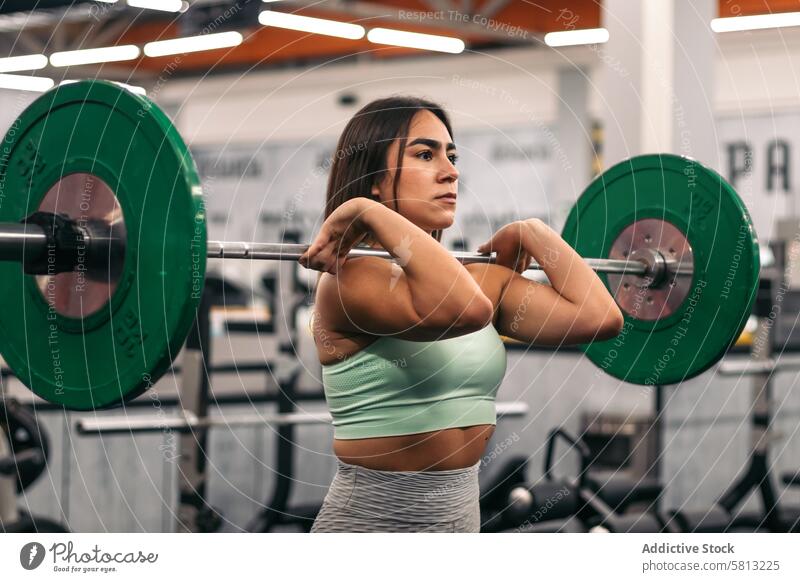 Konzentrierte Sportlerin hebt eine Langhantel während eines Krafttrainings im Fitnessstudio und schaut dabei weg muskulös Stärke Frau Curl-Hantel Körper