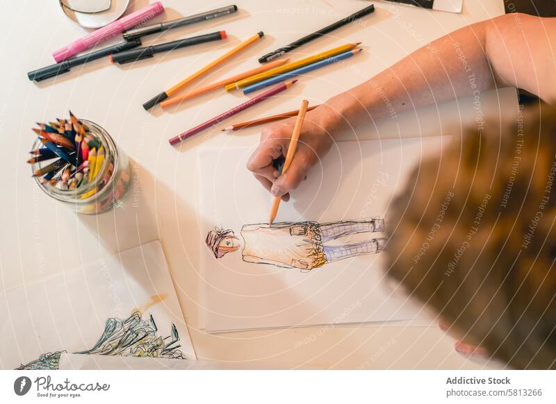 Draufsicht auf einen Modedesigner, der eine Modeskizze mit bunten Bleistiften zeichnet 50s oben Bekleidung Selbstvertrauen selbstbewusst Kreativität Design