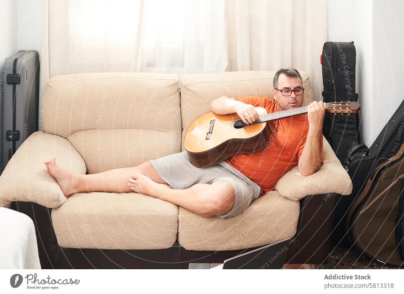 ein Mann, der sich auf der Couch entspannt und Gitarre spielt Laptop online Schulunterricht Lernen Oberschwingungen Spaß Lieder entspannend Liege Spielen