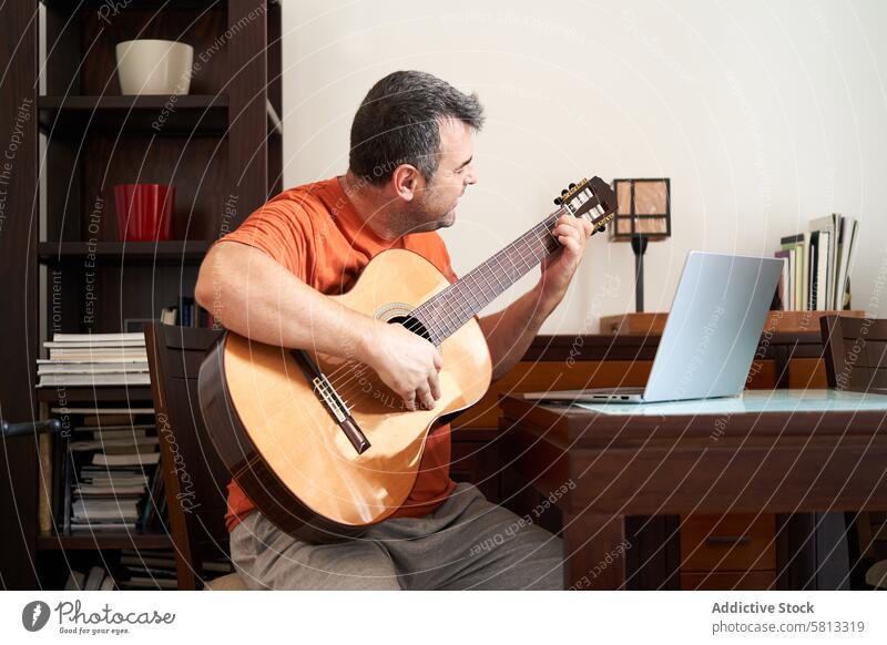 ein Mann mit Laptop im Online-Gitarrenunterricht, der Akkorde lernt Computer online Klassik Klasse Schulunterricht Lernen Gitarrenspieler Musiker Musical Sitzen