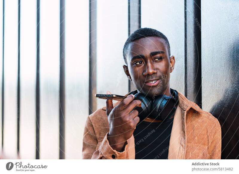 Schwarzer Mann mit Kopfhörern, der eine Sprachnachricht aufnimmt Smartphone Stimme Nachricht Audio meloman Wand Straße Aufzeichnen Großstadt benutzend Anschluss
