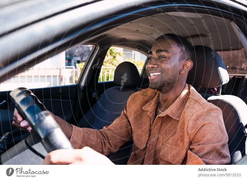 Fröhlicher schwarzer Mann im Auto PKW Fahrer Automobil Laufwerk Lächeln Arbeitsweg Vorschein Fenster Straße Lenkrad positiv Afroamerikaner Verkehr modern