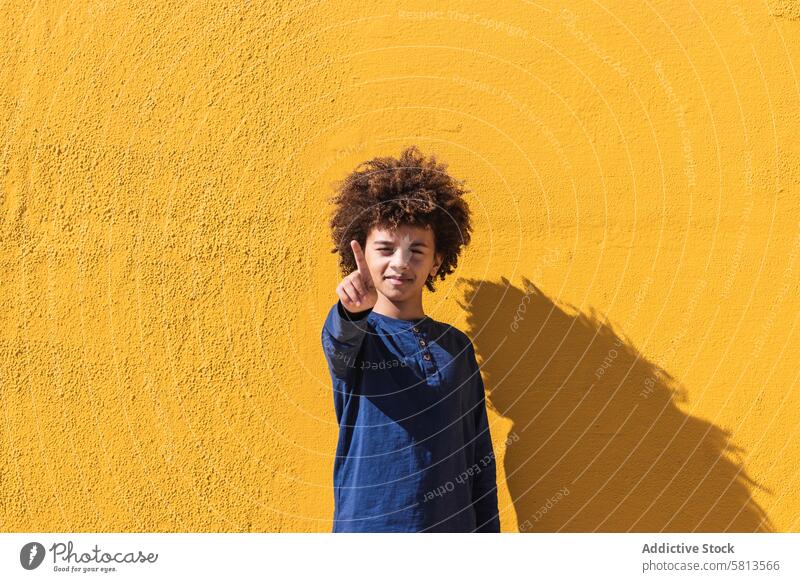 Ethnischer Junge mit lockigem Haar, der auf die Kamera zeigt Afro-Look krause Haare auf die Kamera zeigen farbenfroh hell Kind Teenager Finger gestikulieren
