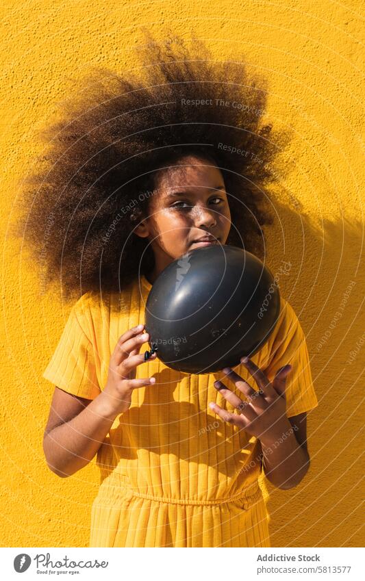 Schwarzes Mädchen hält Party Ballon Luftballon schwarz gelb Afro-Look krause Haare farbenfroh Farbe lebhaft aufblasen Kind Teenager Frisur ethnisch