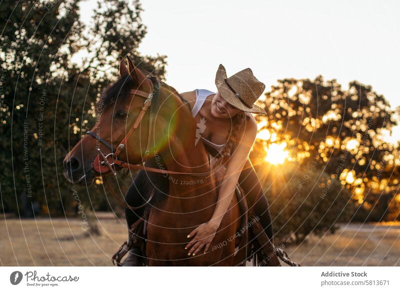 Junge Frau mit Hut reitet auf einem Pferd in der Landschaft bei Sonnenuntergang Natur jung Tier Ranch Cowgirl Cowboy Person pferdeähnlich Reiten schön Reiterin