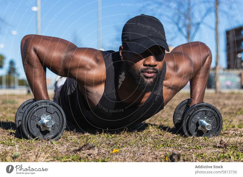 Starker afroamerikanischer Sportler beim Hantelstemmen in der Stadt hochschieben Kurzhantel Fitness Training Muskel Aktivität Rasen Mann Bizeps Gras Athlet