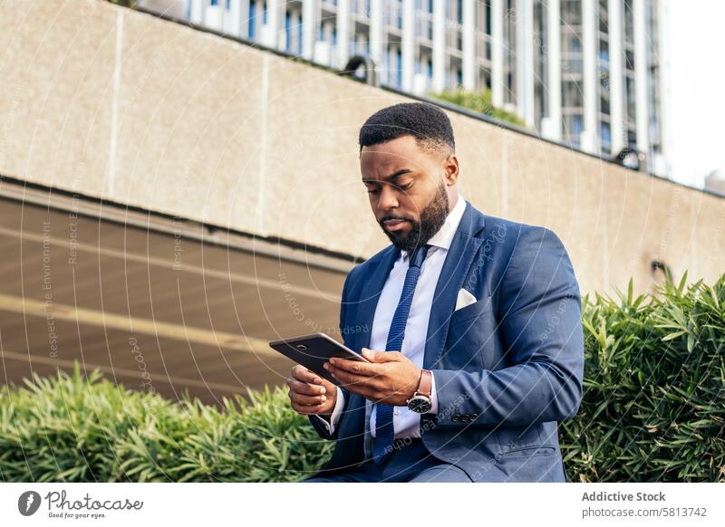 Tiefblick auf einen schwarzen Geschäftsmann im Anzug, der draußen ein Tablet benutzt. Er sieht konzentriert aus Business Sitzung Team professionell Exekutive