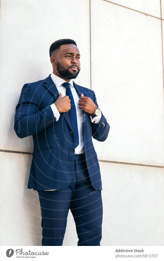 Porträt eines schwarzen Geschäftsmannes in einem Anzug, der seinen Blazer selbstbewusst zurechtrückt Afroamerikaner Mann männlich Business professionell