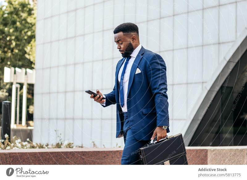 Schwarzer Geschäftsmann im Anzug verlässt das Büro, hält seine Arbeitsmappe und benutzt sein Smartphone Business Sitzung Team professionell Exekutive Erfolg