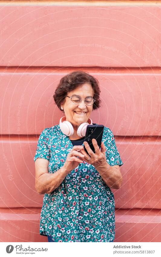 Alte Frau, die ein Smartphone benutzt und mit Kopfhörern Musik hört stylisch Mobile Funktelefon Senior Mitteilung Gerät Nachricht Lifestyle Internet Handy alt