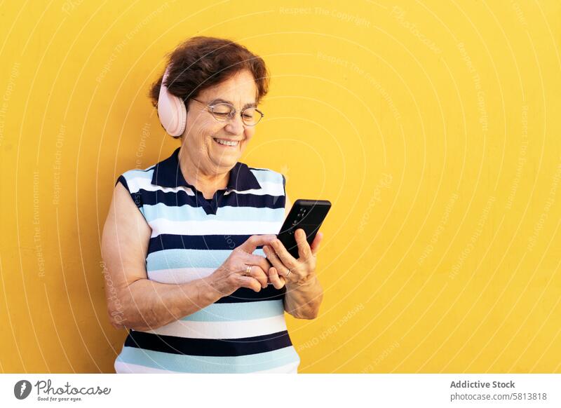 Alte Frau, die ein Smartphone benutzt und mit Kopfhörern Musik hört stylisch Mobile Funktelefon Senior Mitteilung Gerät Nachricht Lifestyle Internet Handy alt