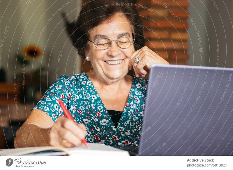 Alte Frau mit Brille, die zu Hause einen Laptop und ein Notizbuch benutzt Senior Technik & Technologie Computer reif Glück heimwärts Internet Person Menschen