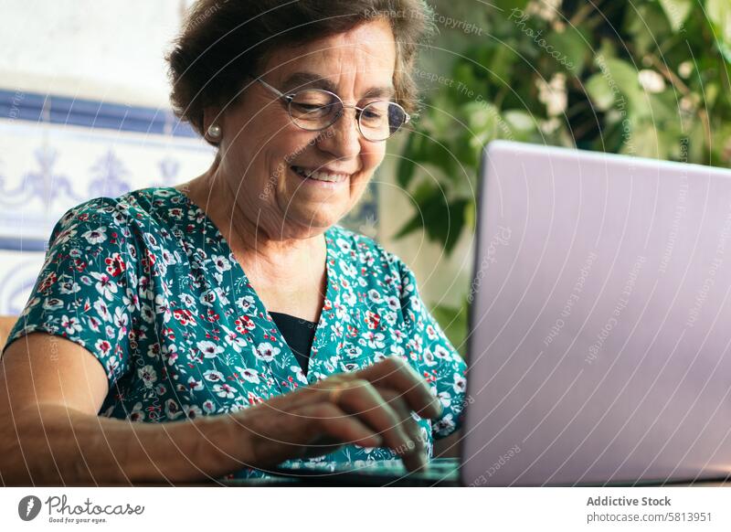 Ältere Frau mit Brille benutzt zu Hause einen Laptop und ein Notebook Senior Technik & Technologie Computer reif Glück heimwärts Internet Person Menschen Sitzen