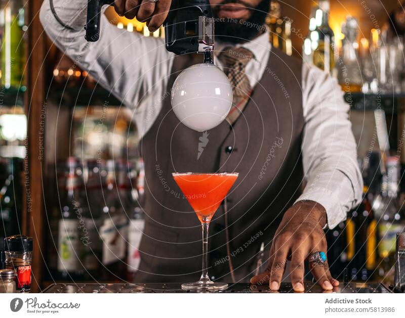 Stilvoller schwarzer Barkeeper bei der Zubereitung eines Cocktails mit einer Rauchblase in einer traditionellen Cocktailbar Barmann Getränk Mixologe Nachtclub