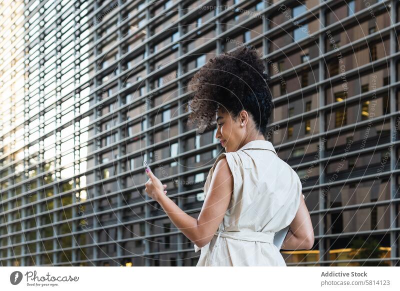 Schwarze Frau mit Laptop, die ihr Smartphone überprüft benutzend prüfen zuschauen Internet online Suche Browsen achtsam Gerät Gebäude Surfen modern Funktelefon