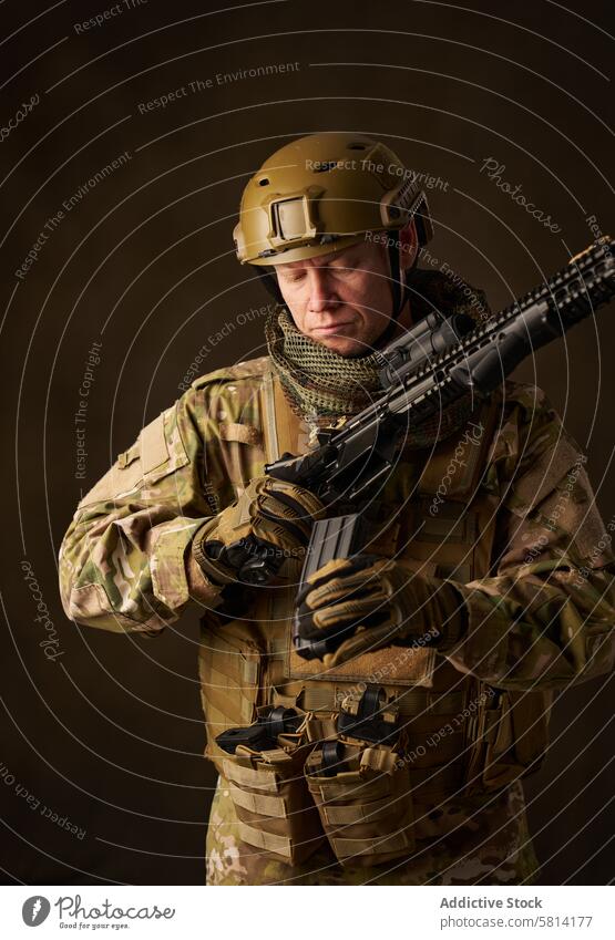 Junger Militärsoldat lädt ein automatisches Airsoft-Gewehr mit Zielfernrohr nach Mann Outfit Genuss Hobbys Simulation Spiel jung Soldat ausfahrbar Sehvermögen