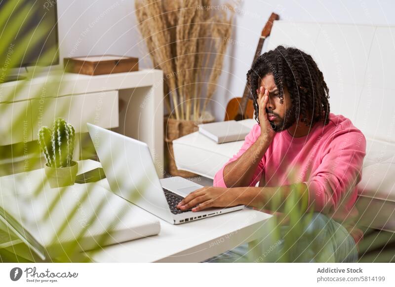 besorgter und deprimierter Mann, der von zu Hause aus arbeitet und sein Gesicht mit den Händen vor dem Laptop verdeckt beunruhigt jung arbeiten heimwärts