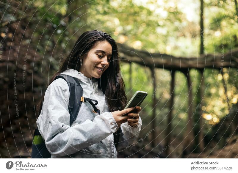 Fröhliche Frau benutzt Smartphone im Dschungel Wald Porträt im Freien Natur Lifestyle Menschen Urlaub Freizeit Blick wandern Baum reisen Rucksack Herbst