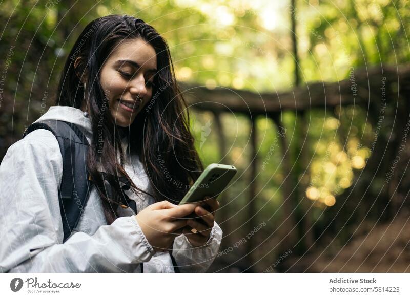 Junge Frau schreibt eine SMS im Wald Porträt im Freien Natur Lifestyle Menschen Urlaub Freizeit Blick wandern Baum reisen Rucksack Herbst Abenteuer Nahaufnahme