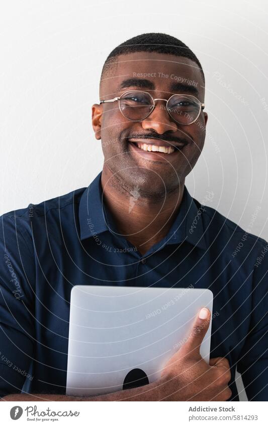 Lächelnder schwarzer Mann mit Laptop in der Nähe einer weißen Wand Netbook Glück gut gekleidet Zeitgenosse positiv Brille Studioaufnahme Afroamerikaner