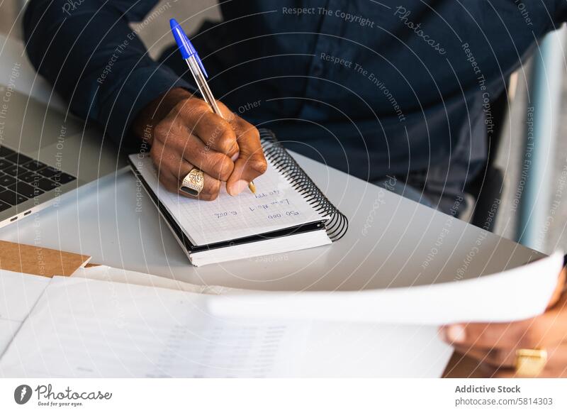 Afroamerikanischer Mann, der in der Nähe eines Laptops im Büro in einen Notizblock schreibt zur Kenntnis nehmen Notebook Netbook Tisch Schriftstück