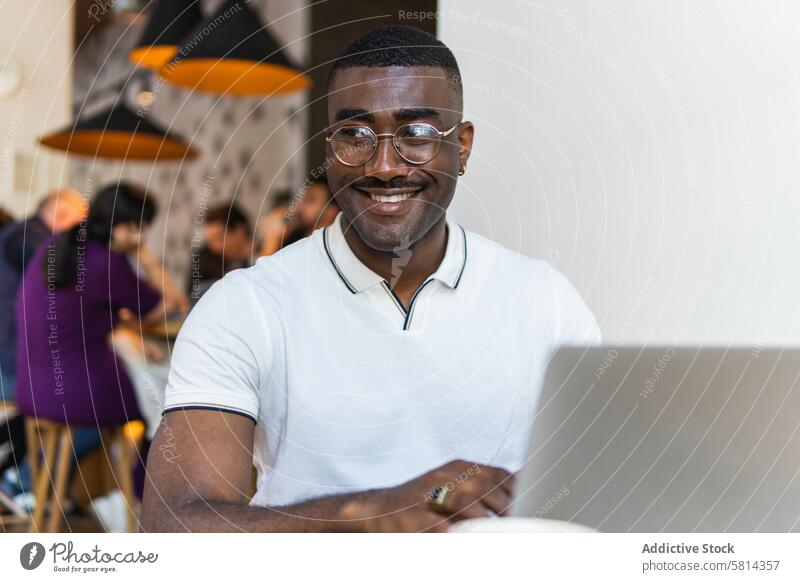 Afroamerikanischer Mann mit Laptop am Tisch in einem Café Tasse trinken Brille modern Afroamerikaner schwarz männlich Erwachsener online Computer Lifestyle