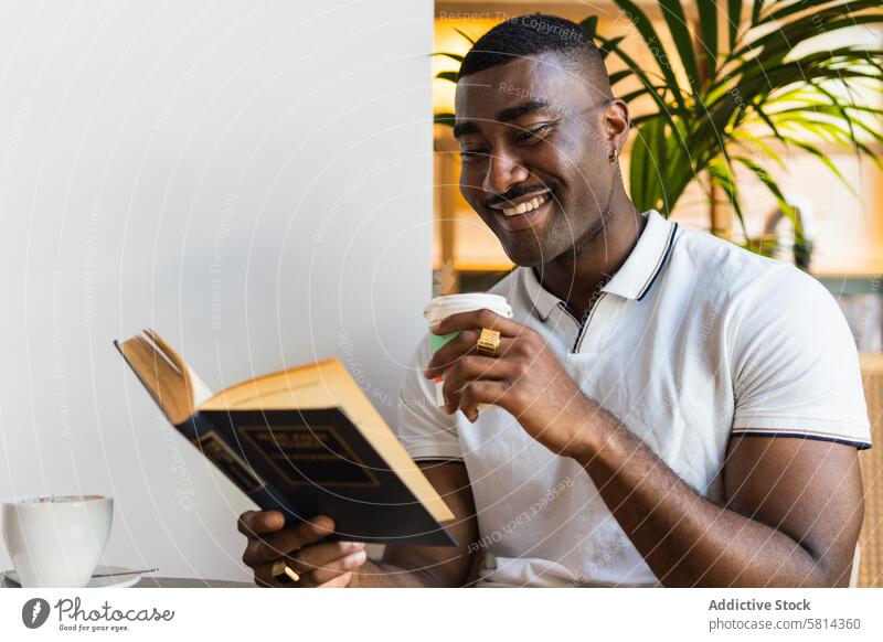 Lächelnder afroamerikanischer Mann, der mit einem Getränk im Café ein Buch liest Pappbecher trinken allein Tasse Tisch Glück Afroamerikaner schwarz männlich
