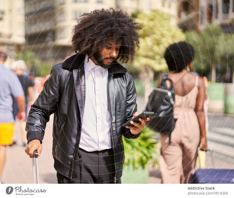 ein junger Mann mit Afro-Haar in der Stadt mit einem Koffer und einem Handy laufen ringsherum Großstadt benutzend Mobile Telefon Reisen Person Ausflug Gepäck
