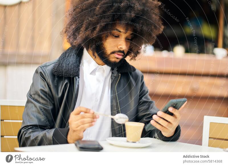 ein afrikanisch-amerikanischer Mann schaut auf sein Handy, während er Kaffee trinkt Porträt Afro-Look Behaarung habend heiß Terrasse Blick Zelle Telefon trinken