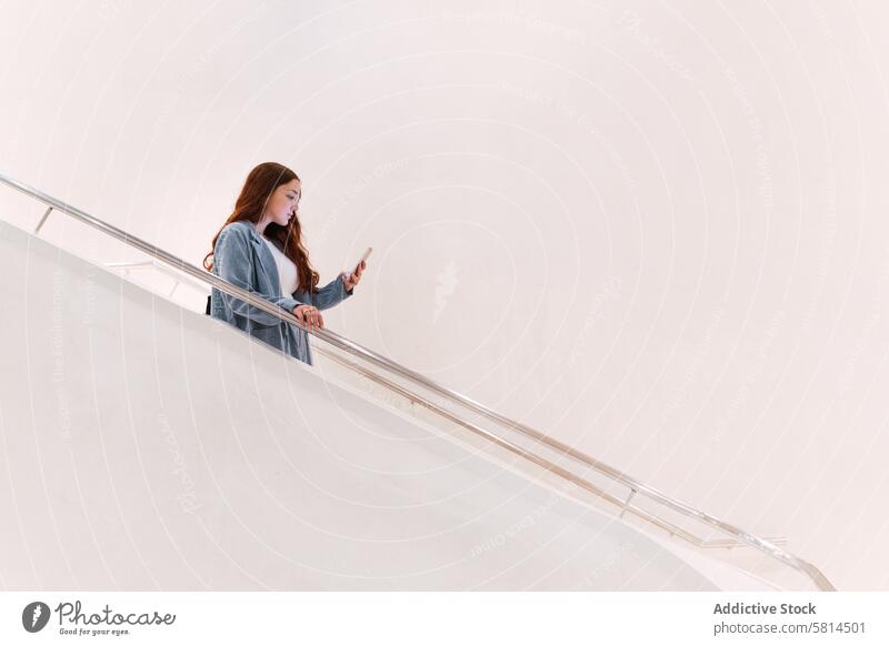Frau, die auf einer Treppe ihr Smartphone durchsucht Treppenhaus Browsen online Textnachricht Talkrunde Stil modern elegant Design Gang Saal Mode trendy App