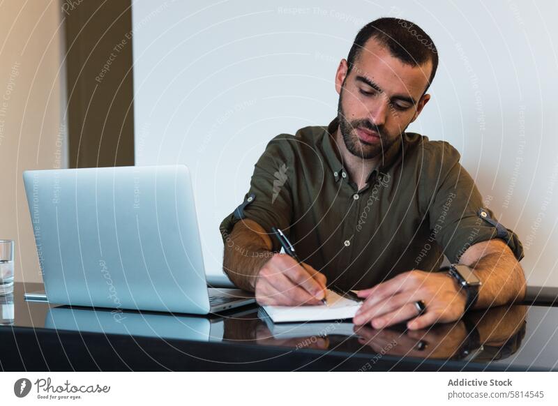 Mann schreibt in Notizbuch neben Laptop zur Kenntnis nehmen Notebook Notizblock schreiben Arbeit Arbeitsplatz Erinnerung Aufgabe Netbook männlich Tisch Gerät