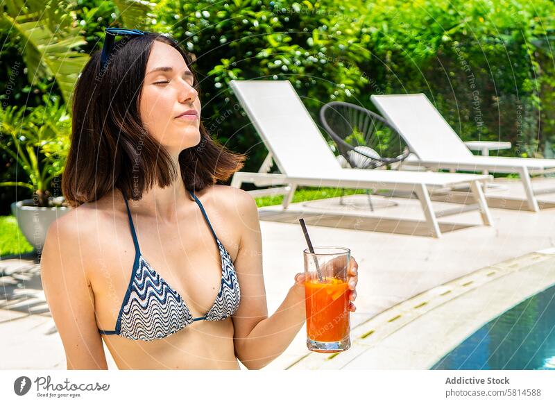 Schöne Frau, die sich am Pool mit einem Saft in der Hand entspannt. Erwachsener attraktiv schön Schönheit Getränk Bikini sorgenfrei Kaukasier Stuhl charmant