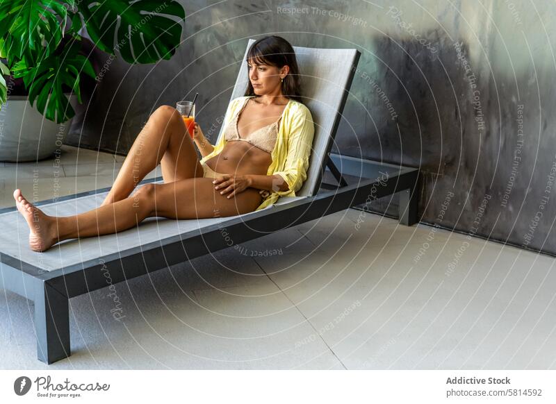 Eine schöne Frau ruht sich auf einem Liegestuhl im Poolbereich eines schicken Hotels aus. Raum kopieren Erwachsener attraktiv Schönheit Getränk Bikini