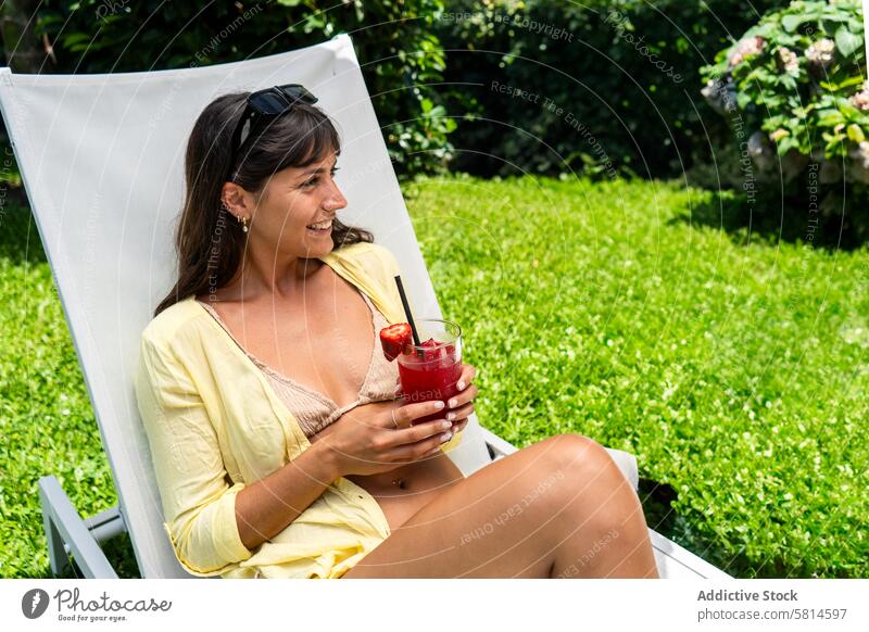Schöne Frau entspannt sich auf einem Liegestuhl mit einem Saft in der Hand. Erwachsener attraktiv schön Schönheit Getränk Bikini sorgenfrei Kaukasier Stuhl
