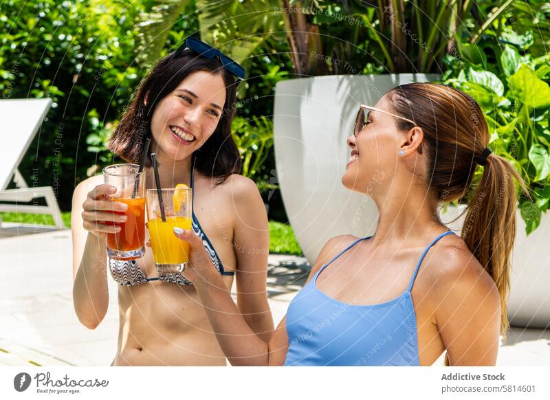 Zwei Freunde sitzen an einem Swimmingpool, jeder hält einen Fruchtsmoothie in der Hand. attraktiv schön beste Getränk Bikini Bonden sorgenfrei Stuhl Hof