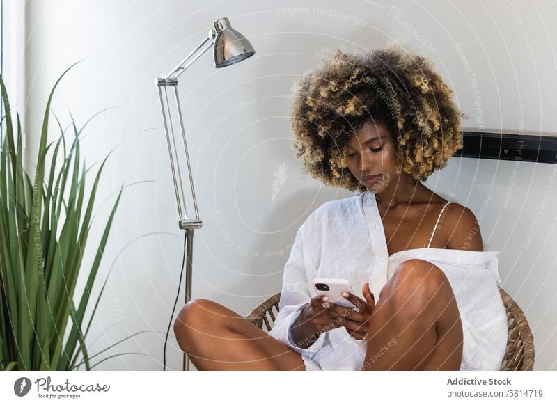 Schwarze Frau benutzt Smartphone im Korbsessel Nachricht Internet zuschauen benutzend Morgen ernst Anschluss digital Browsen Surfen Apparatur Mobile Armsessel