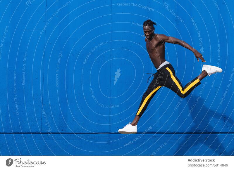 Fröhlicher schwarzer Mann springt auf die Straße heiter springen laufen sportlich Glück Energie ohne Hemd Athlet jung Sportler Afroamerikaner ethnisch Regen