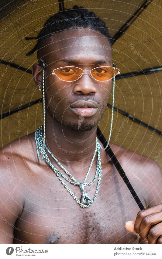 Stilvoller schwarzer Mann ohne Hemd mit Regenschirm Sonnenbrille trendy Accessoire Mode ernst Porträt selbstbewusst ethnisch jung Afroamerikaner nackter Torso
