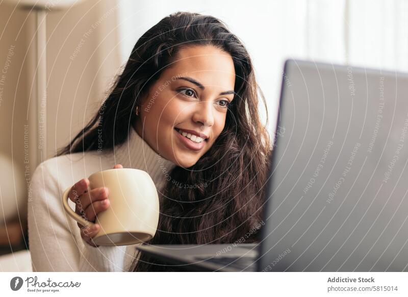 Junge Frau, die eine Tasse Kaffee genießt und einen Laptop benutzt Sofa heimwärts Technik & Technologie Produktivität abgelegen Anschluss Drahtlos modern