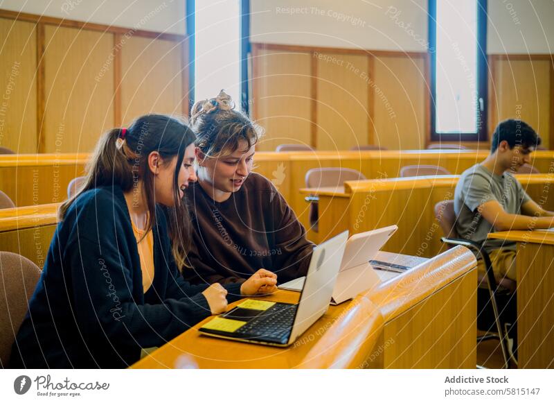 Team von Studentinnen sitzt am Schreibtisch mit Laptop und Tablet Frauen Schüler Tablette lernen Bildung diskutieren Lächeln Kommunizieren Klassenraum jung