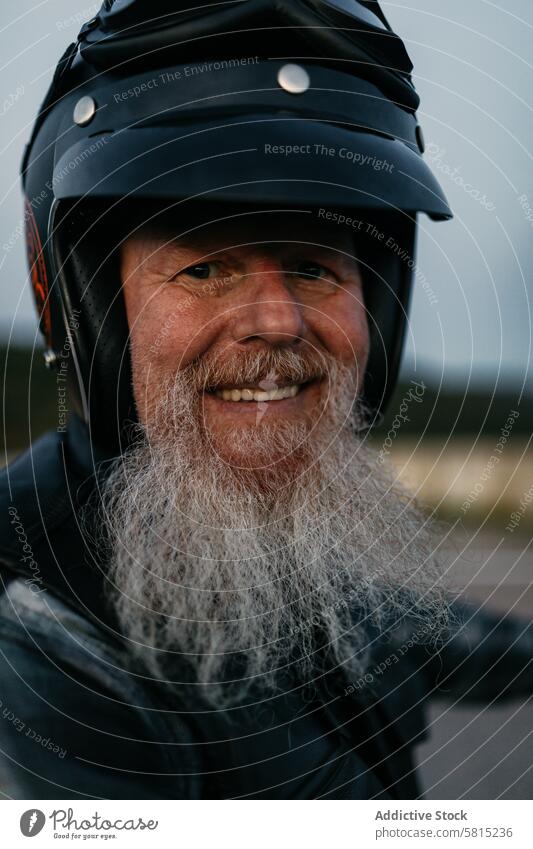Lächelnder älterer Biker mit Helm und Lederjacke Senior Mann Schutzhelm Motorrad in die Kamera schauen Reiter Porträt heiter Vollbart weißer Bart Glück