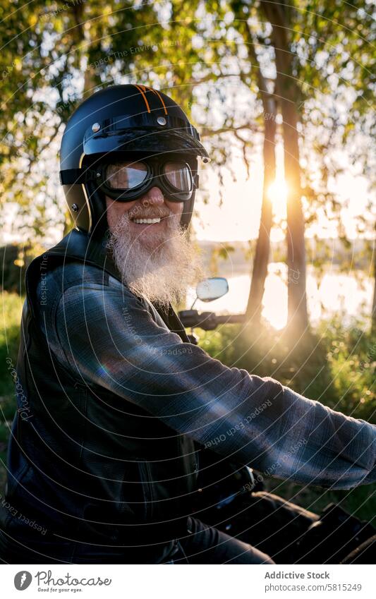 Älterer Biker genießt Sonnenuntergang Fahrt auf Motorrad Senior Mitfahrgelegenheit älter männlich Vollbart Lächeln Glück Schutzhelm Schutzbrille Lederjacke