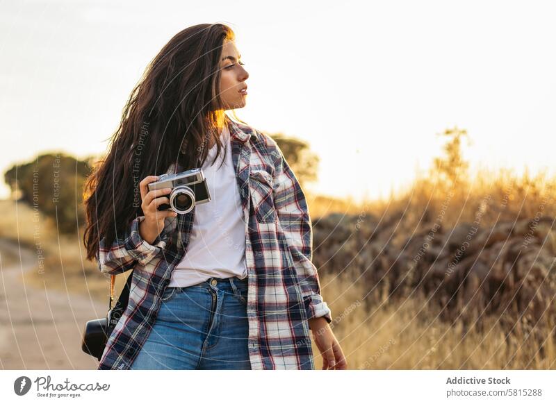 Junge Frau, die mit einer analogen Kamera im Feld bei Sonnenuntergang fotografiert Foto Lifestyle jung Mädchen Fotografie altehrwürdig Fotokamera retro reisen