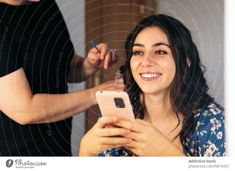 Junge spanische Frau benutzt ihr Smartphone bei einer Haar- und Make-up-Behandlung Model Spiegel Schönheit Künstler jung schön Blick Gesicht Glamour Kosmetik