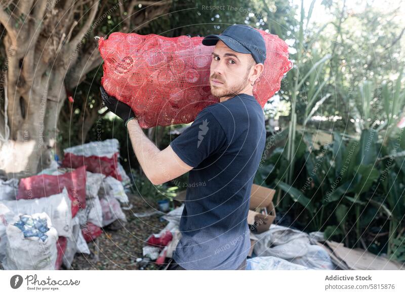 Junger kaukasischer Mann, der in einer Recyclinganlage mit recycelten Glasflaschen hantiert. Ernsthafte Haltung jung Kaukasier Handhabung Sack wiederverwertet