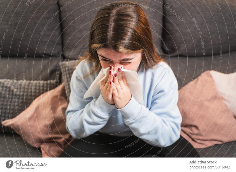 Junge Frau mit einer Erkältung sitzt zu Hause auf einer Couch kalt Gewebe Liege heimwärts Krankheit Sitzen blasende Nase Allergie im Innenbereich jung